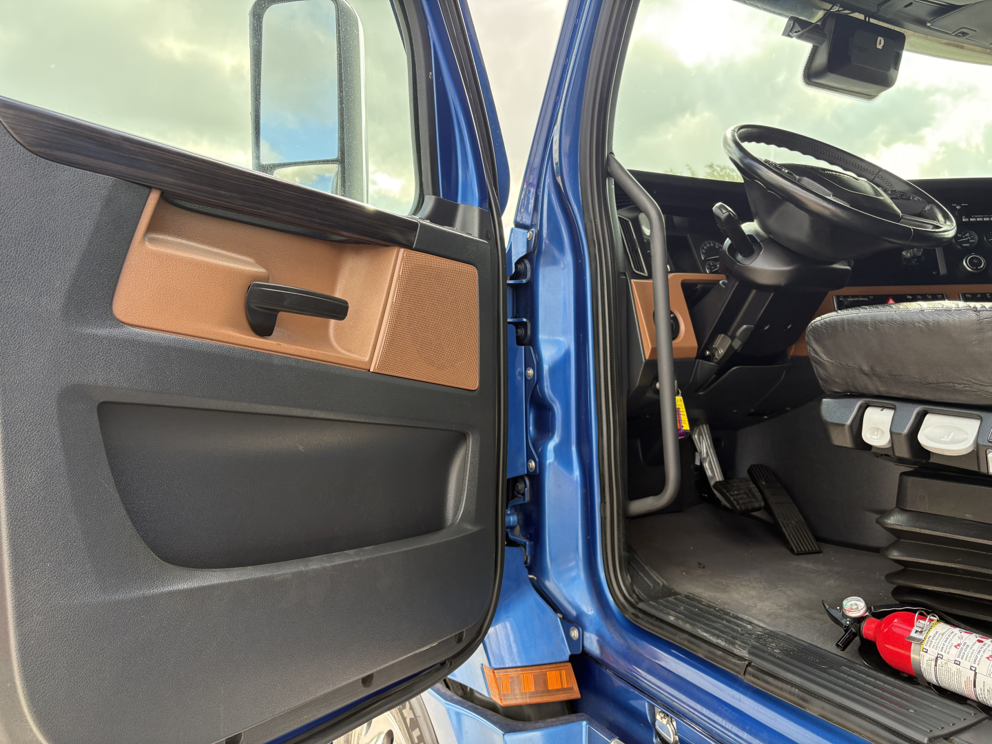 Truck cab interior door and driver's seat area of a blue Freightliner Cascadia 126; visible text includes vehicle details in listing: VIN, stock number, category, type, used status.