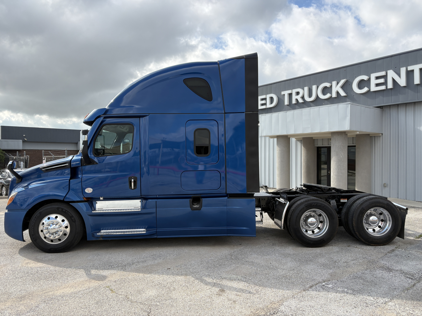 Truck side view of a blue 2022 Freightliner Cascadia 126 conventional sleeper tractor showing cab and tandem rear axles.