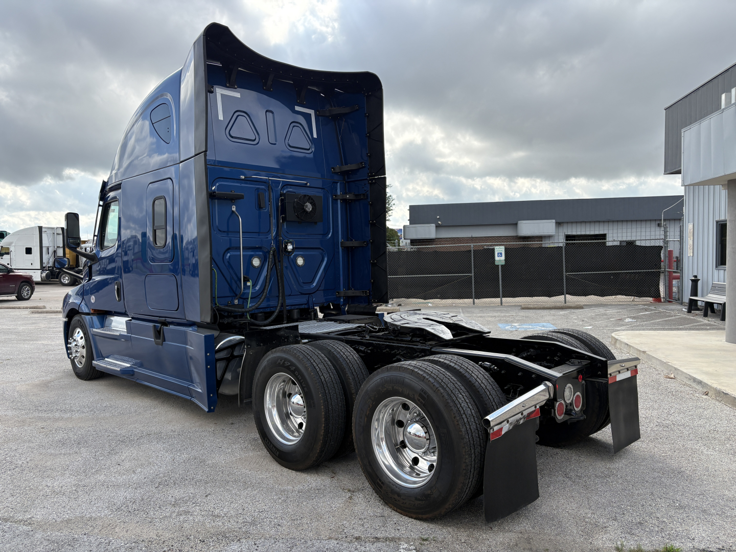 Truck chassis of a blue 2022 Freightliner Cascadia 126 tractor, rear view showing dual rear axles with polished aluminum wheels and black trailer mud flaps.