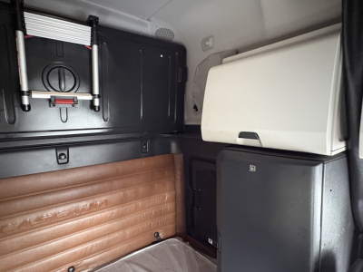 Cab interior of a 2022 Freightliner Cascadia 126 sleeper showing storage compartments, white cabinet, and brown padded window area.