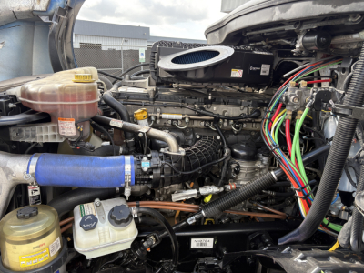 Engine bay of a 2022 Freightliner Cascadia 126 showing coolant reservoir, air intake, various hoses, wiring harness, and exposed engine components.