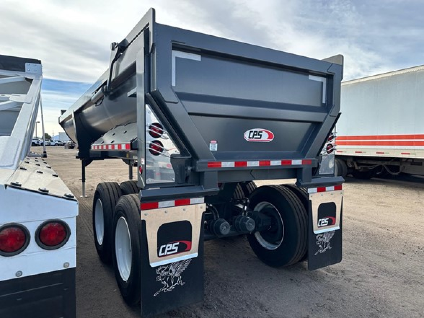Framed dump trailer rear view showing high lift gate and dual rear axles with CPS logo mud flaps and reflective strips.