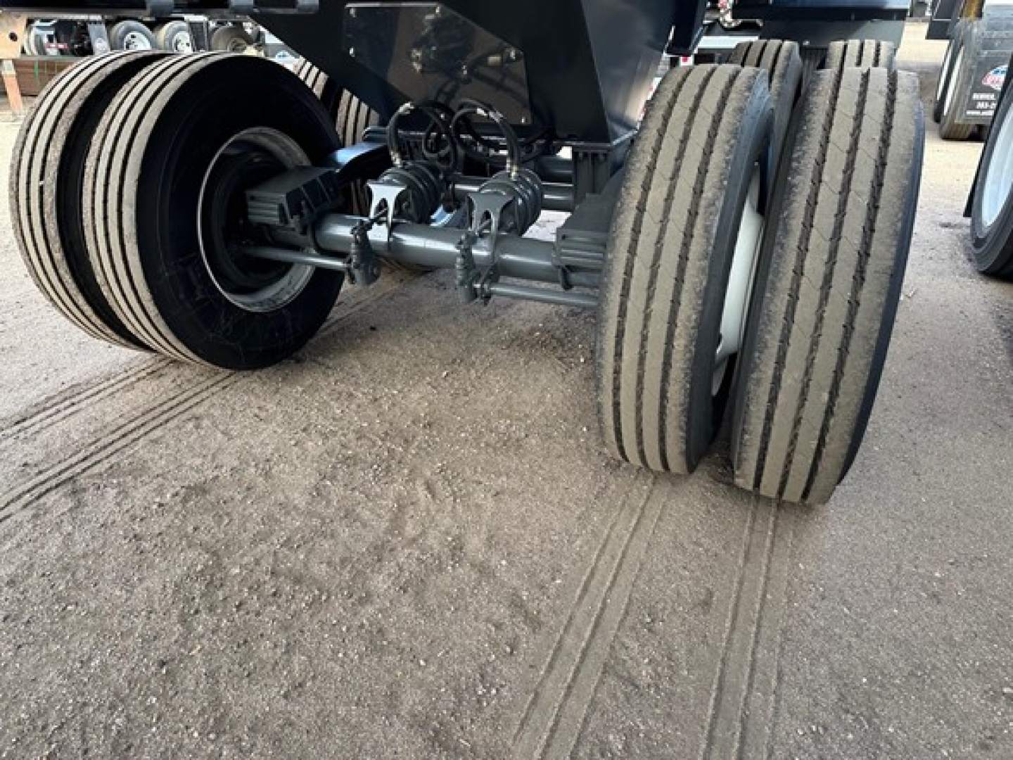 Trailer axles with dual rear wheels and undercarriage components visible; hydraulic lines and suspension hardware on a frameless rock end dump trailer.