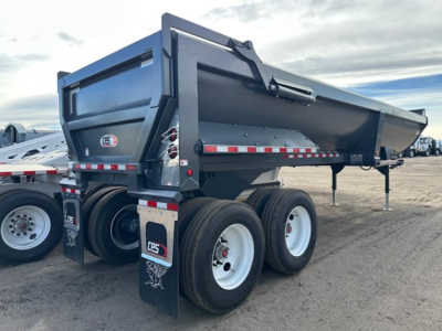 Framed 34' rock end dump trailer with high lift gate, triple-axle configuration, dark gray body, white wheels, and reflective safety stripes visible.