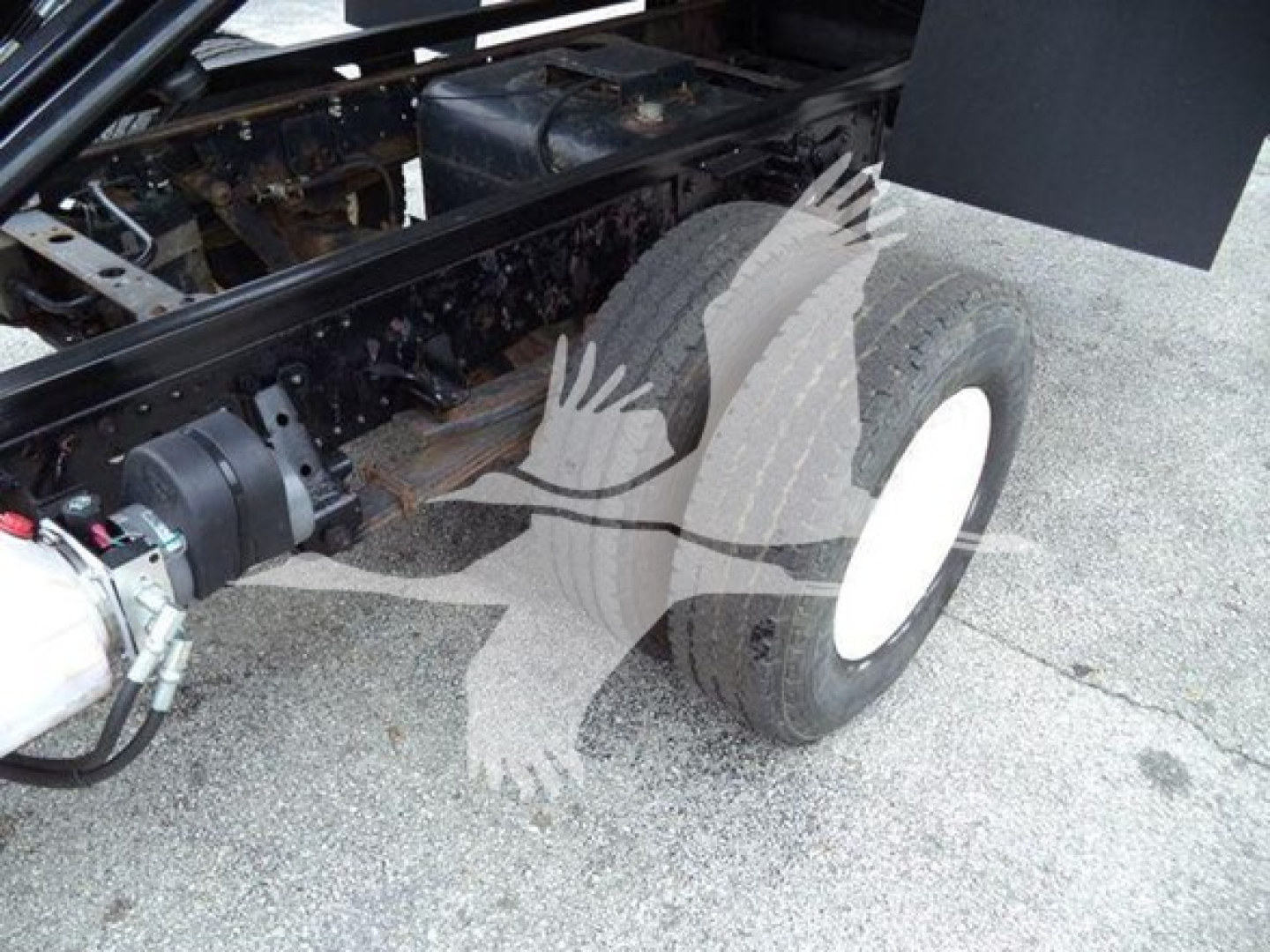 Isuzu NPR dump truck undercarriage showing dual rear wheels and part of drive components with hydraulic line and frame assembly.