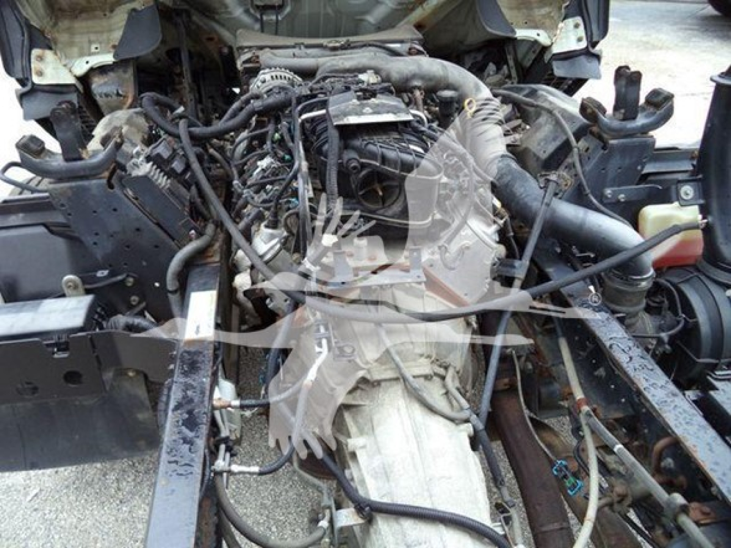 Isuzu NPR diesel truck engine bay/cowl area showing engine with various hoses, belts, and wiring; view from front with radiator support removed.