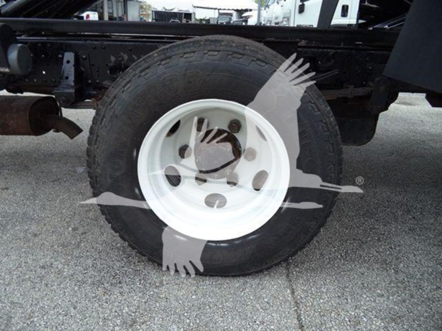 Isuzu NPR chassis showing a single wheel and white steel rim; truck frame and tire visible undercarriage with Suzuki-like branding watermark across image.