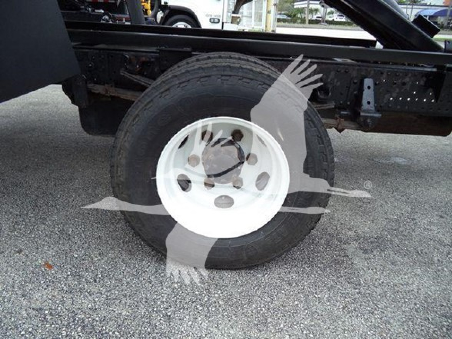 Isuzu NPR dump truck wheel and chassis view showing front tire mounted on white steel rim with black frame undercarriage.