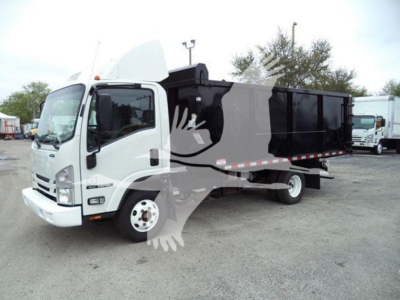 Isuzu NPR dump truck in service showing white cab and black dump bed with raised bed side rails.