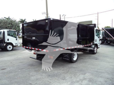 Isuzu NPR dump truck rear/side view showing a black dumped bed with white cab nearby. Visible text includes stock number tag on side and contact numbers.