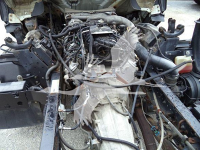 Isuzu NPR diesel truck engine bay/cowl area showing engine with various hoses, belts, and wiring; view from front with radiator support removed.