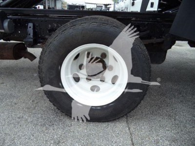 Isuzu NPR chassis showing a single wheel and white steel rim; truck frame and tire visible undercarriage with Suzuki-like branding watermark across image.