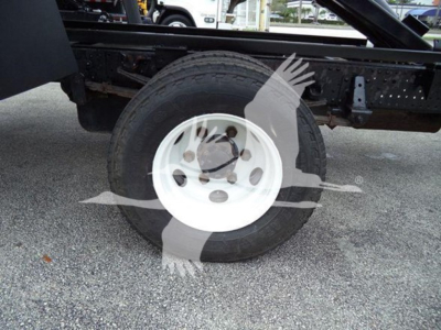 Isuzu NPR dump truck wheel and chassis view showing front tire mounted on white steel rim with black frame undercarriage.