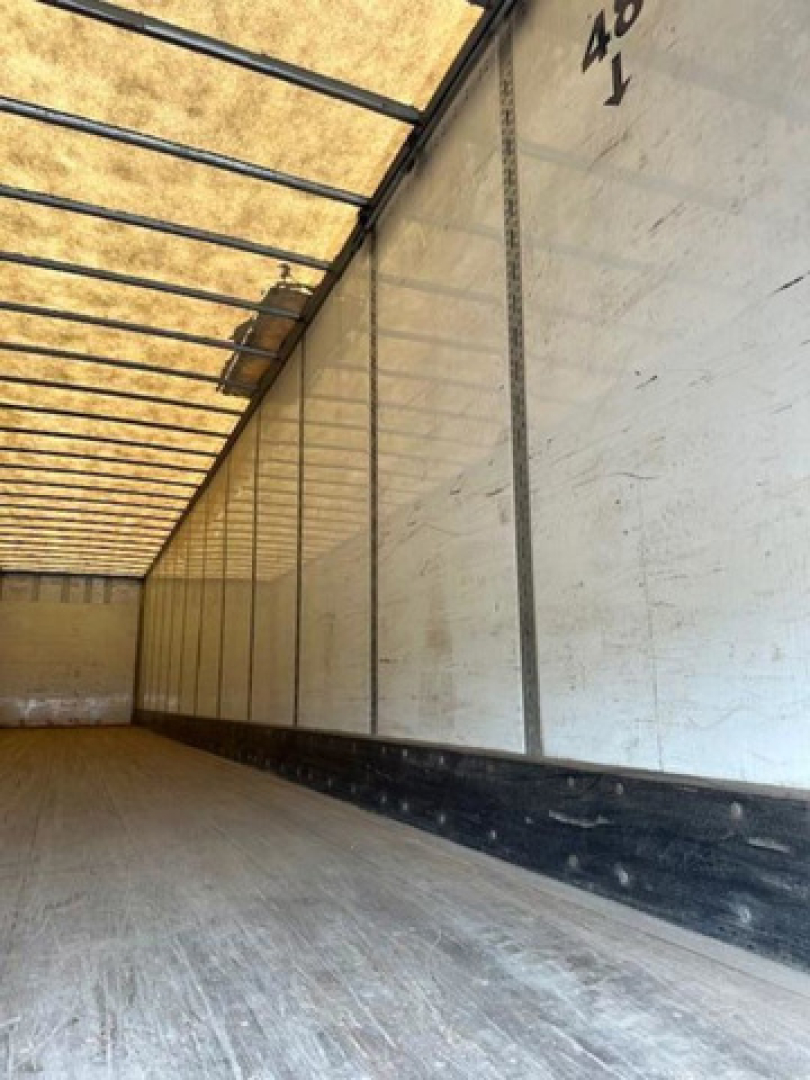 Trailer interior showing empty cargo area with wooden floor and sidewalls, light through top vents.
