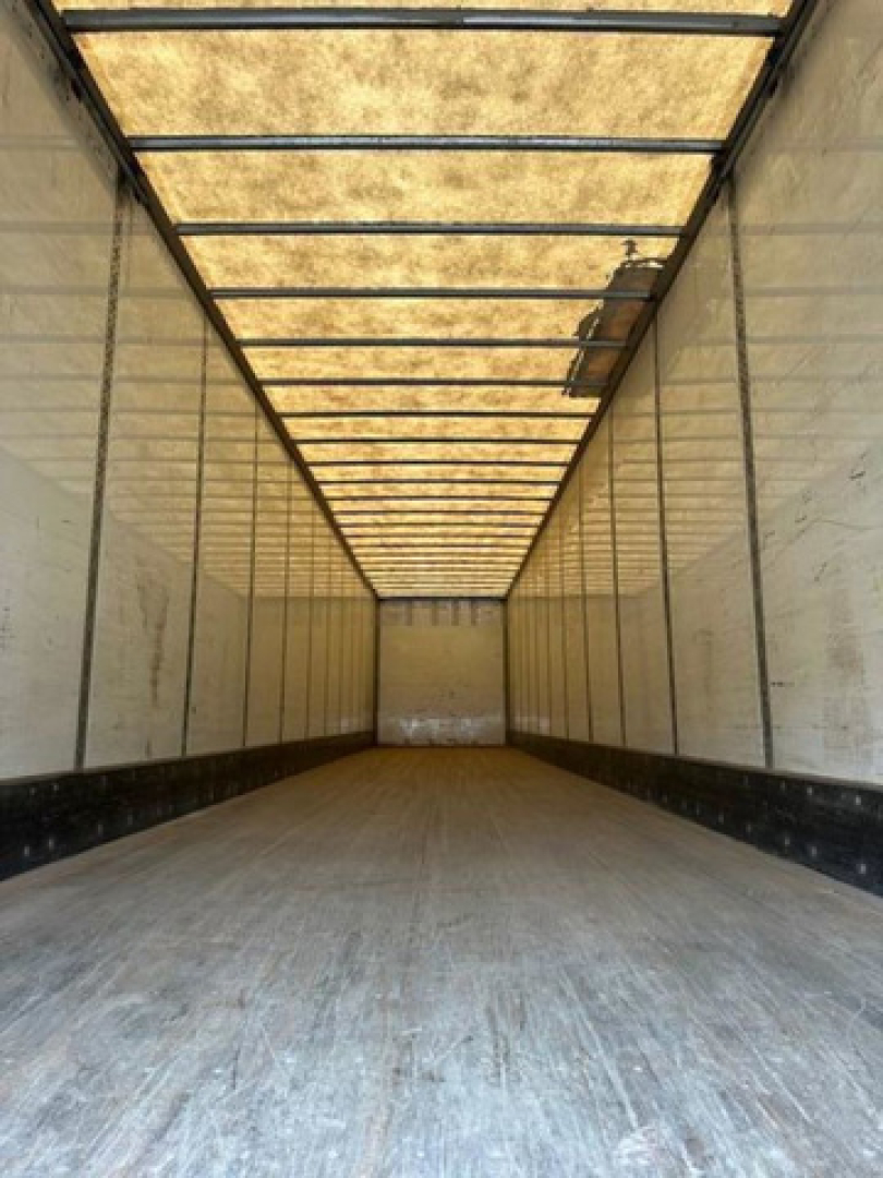 Open empty cargo trailer interior with translucent roof panels and side walls, long rectangular trailer with wooden floor and metal ribs.