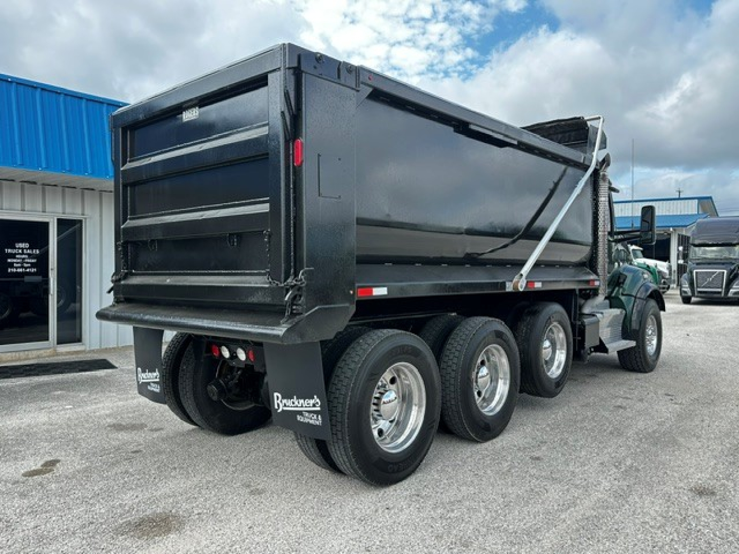 Kenworth T880 dump truck side/rear view showing aluminum tandem rear axles and black dump bed with support chains.