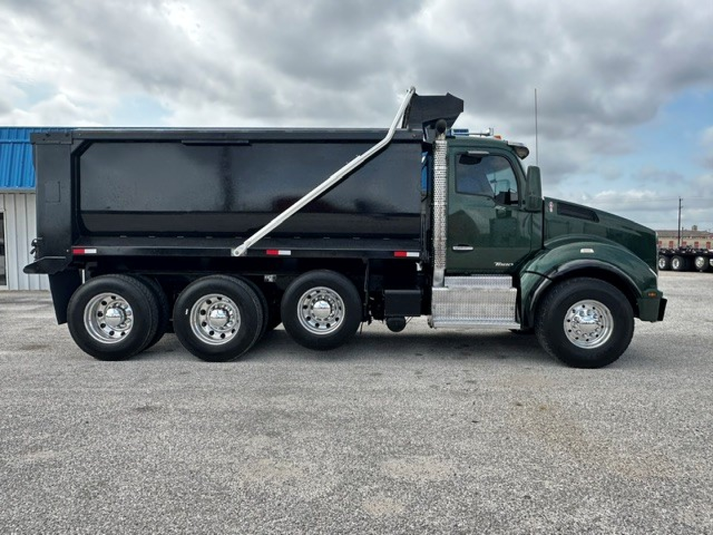 Kenworth T880 dump truck side view showing green cab, six-wheel dump bed, and silver steps with chrome accents.