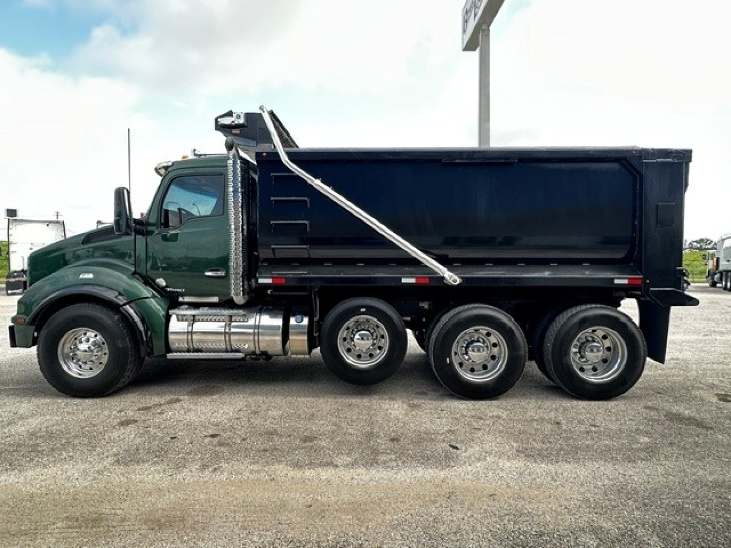 Kenworth T880 dump truck side view showing three-axle rear configuration, dark green cab, black dump body, chrome fuel tanks and exhaust, VIN plate not visible.