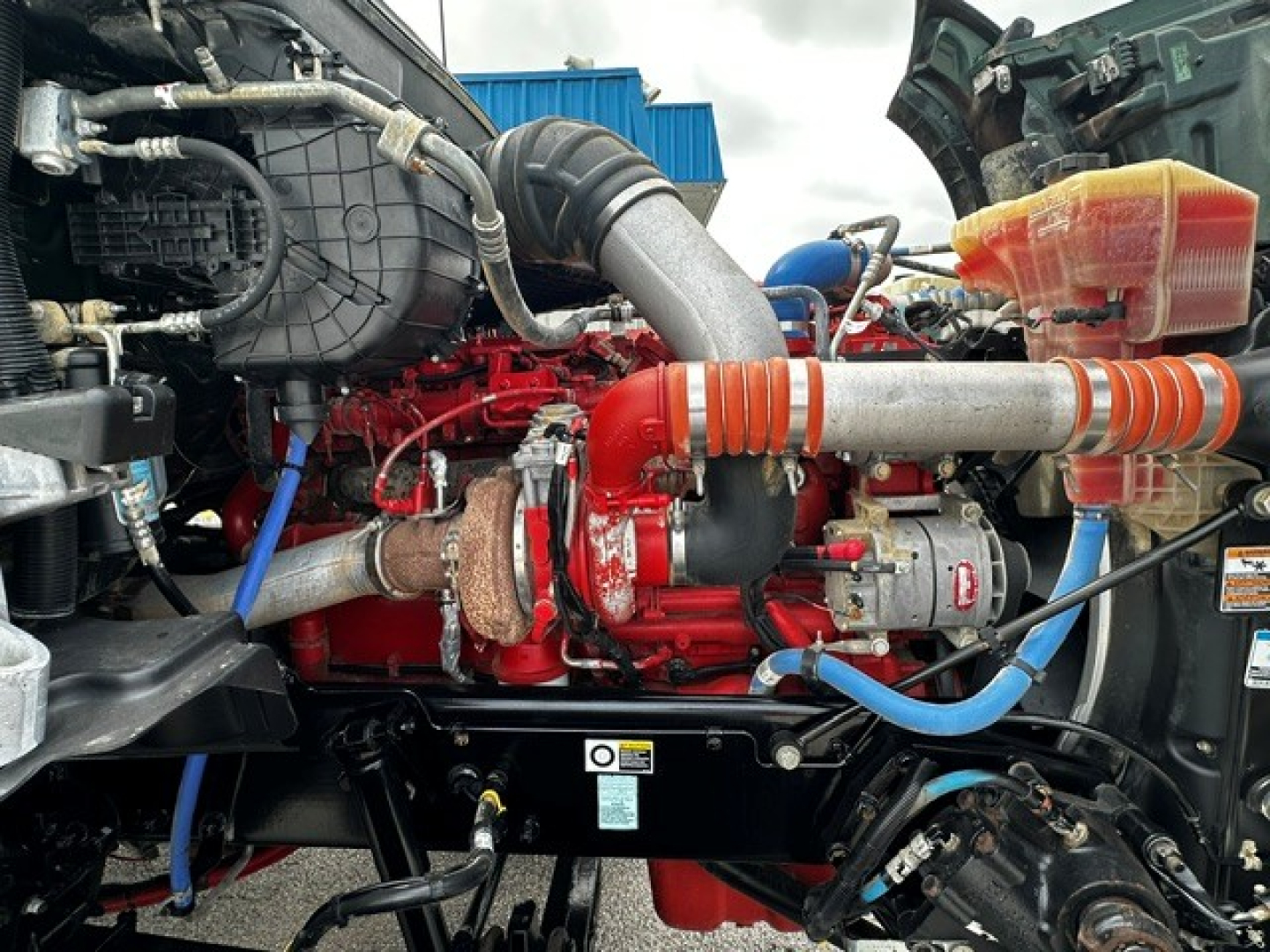 Kenworth T880 engine bay with red engine, silver intake piping, blue hoses, and orange-striped coolant hose visible.