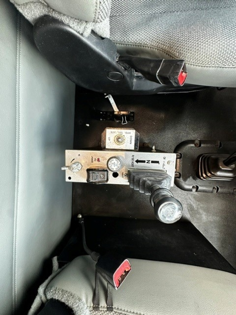 Kenworth T880 interior control panel showing hydraulic control valve with labeled gauges and levers, seat and seatbelt in view.
