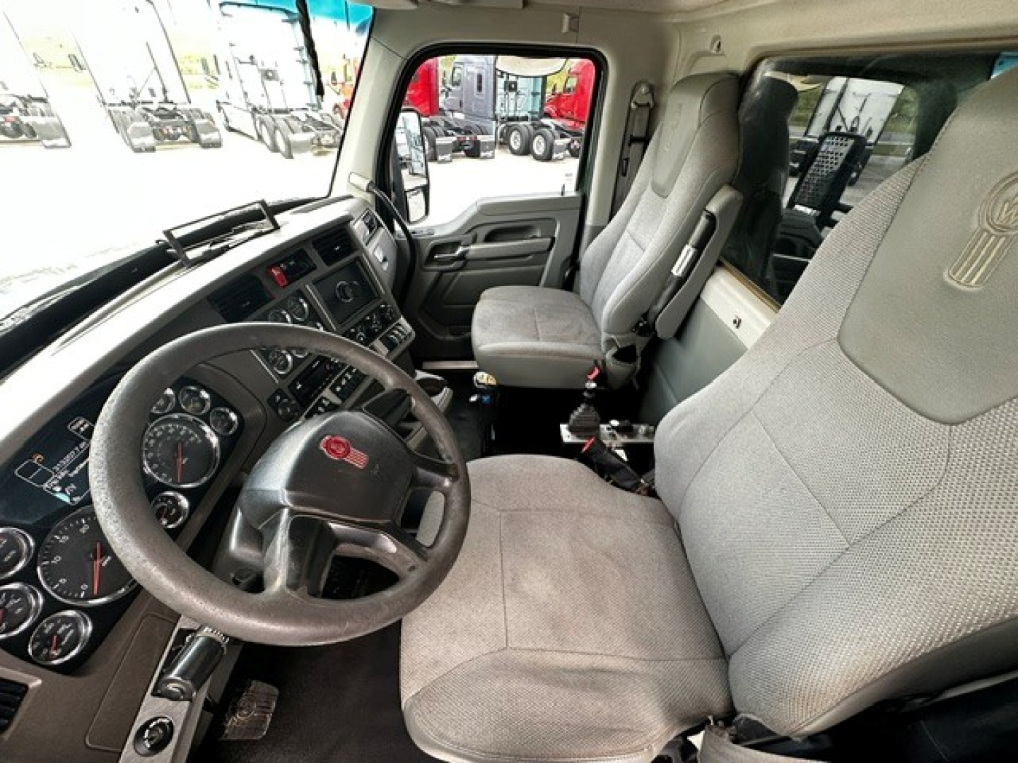 Kenworth T880 truck interior showing steering wheel with Kenworth emblem, front dashboard, and grey cloth seats.