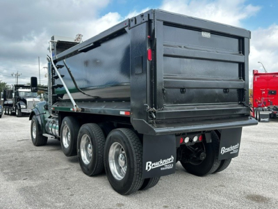 Kenworth T880 dump truck rear and side showing dual rear axles, black dump bed, mud flaps with Bruchner equipment logo, taillights, and rear bumper.