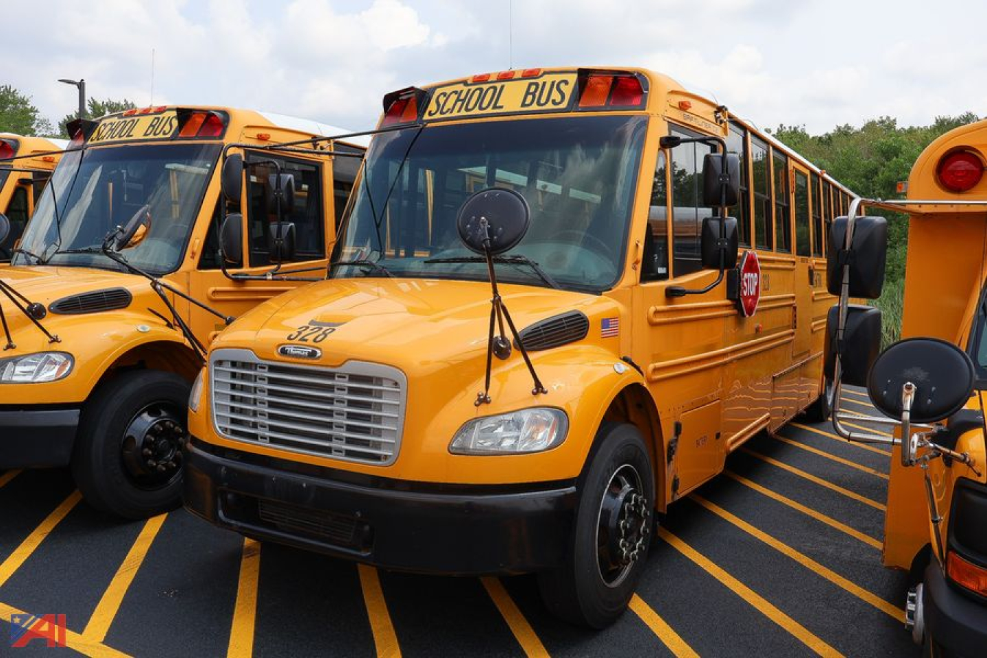 School bus from a row of yellow Freightliner Thomas Saf-T-Liner buses with windshield, mirrors, and ‘SCHOOL BUS’ stop sign visible.