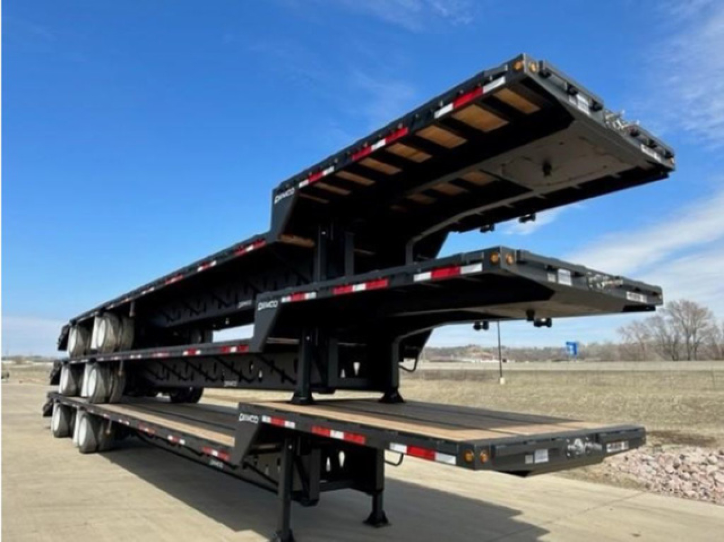 Demco dropdeck trailer stacks with three deployed levels showing metal deck and black frame, side rails, and white and red safety markings.