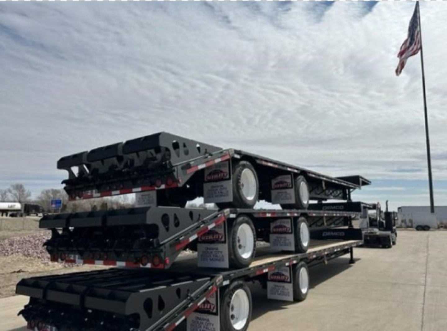 Demco drop deck trailer stack with multiple axles and wheels, showing metal frames and black ramps.