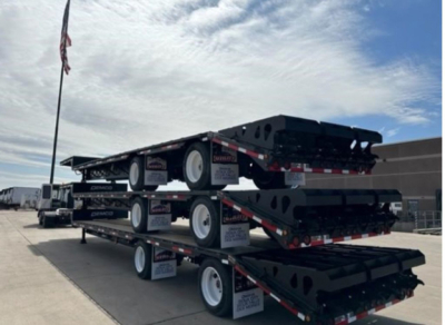Demco dropdeck trailers stacked on a trailer rack showing multiple axles and black frames with white wheels.