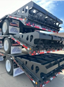Dropdeck trailer stack with multiple metal beams and ramps, side markings and utility decals visible.