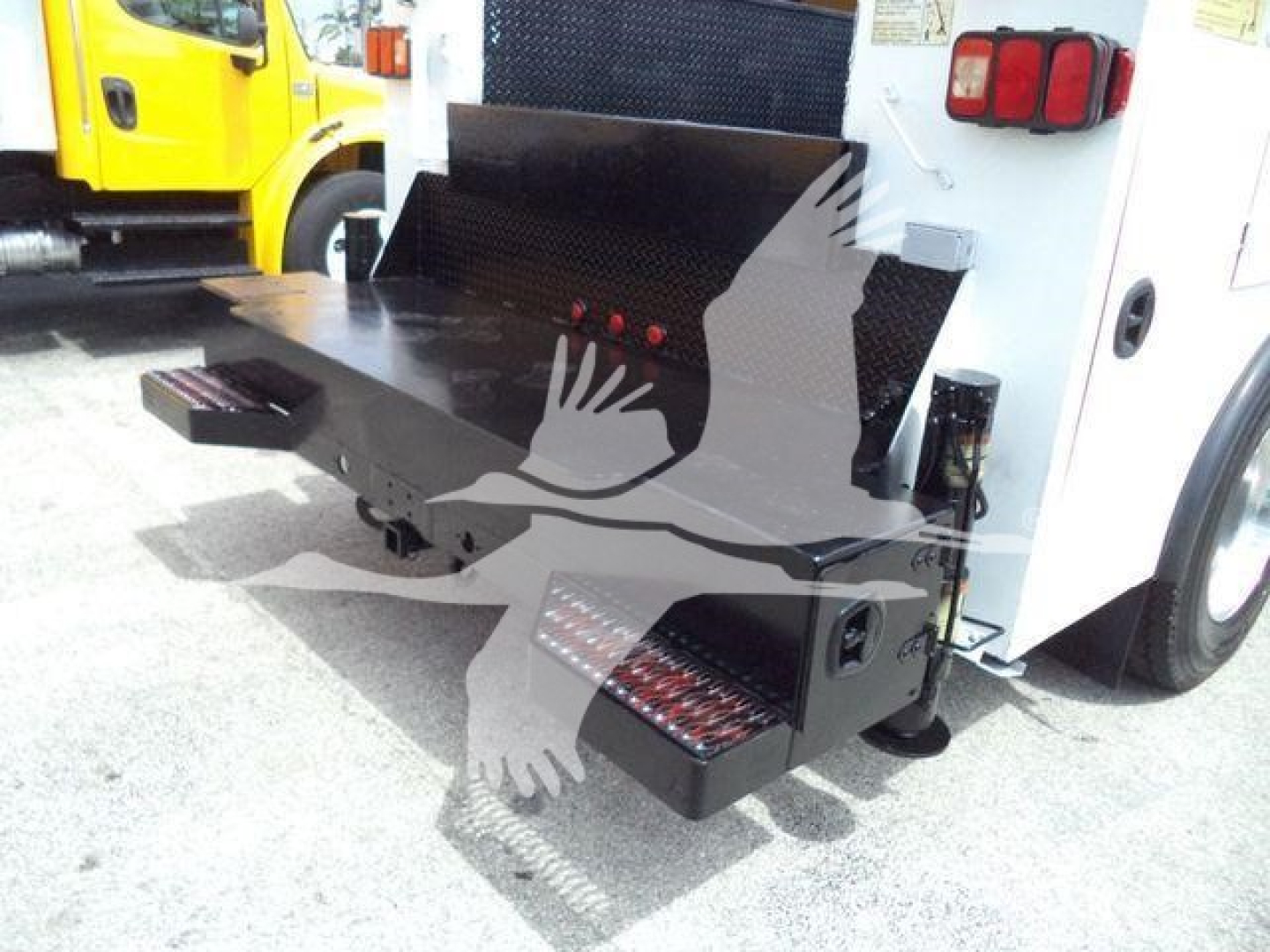 Rear view of a Kenworth service truck with a fold-out stowage step and toolbox, showing a black metal platform and toolbox beneath a rear-mounted bumper.