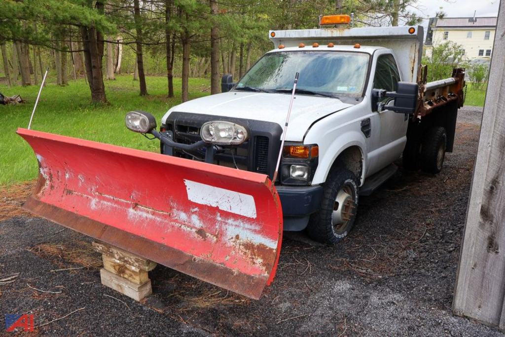Ford F-350 dump truck with plow, front snow plow blade attached, white cab, dump bed, parked on gravel.