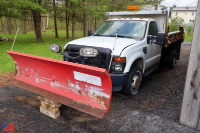 Ford F-350 dump truck with plow, front snow plow blade attached, white cab, dump bed, parked on gravel.