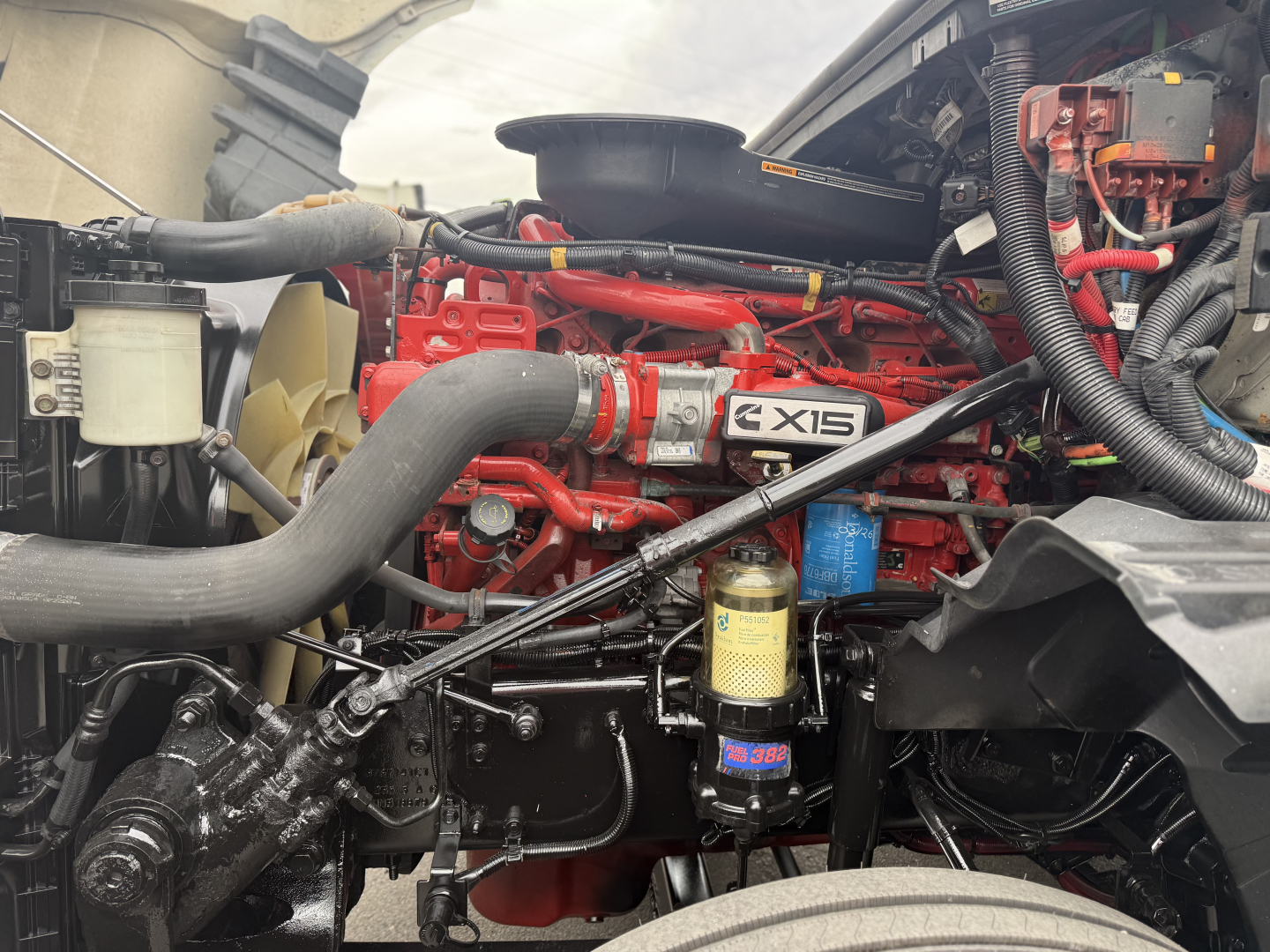 Engine bay of 2021 International LT625 showing EX15 badge, red engine, various hoses, filter canister, and wiring harnesses.