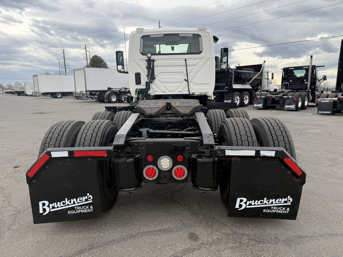 Semi truck rear view showing fifth wheel, dual rear axles, mud flaps with Bruckner's Truck & Equipment logos, and tail lights on a truck lot.