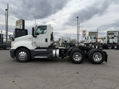 Truck chassis side view showing 2021 International LT625 cab over engine with white cab and black chassis, dual rear axles, highway trailer parking lot.