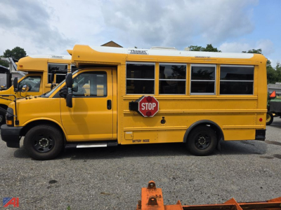 School bus side view showing bright yellow Chevrolet Express school bus with STOP sign and windows, 2019 model in used condition.
