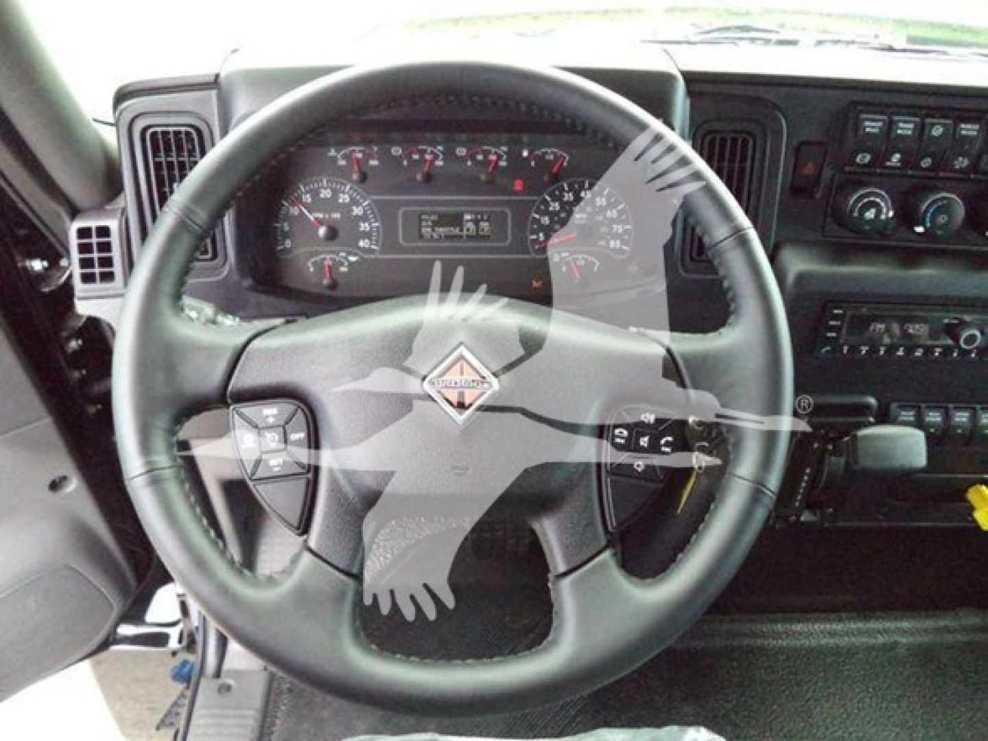 Truck interior showing steering wheel with International logo and dashboard gauges; cockpit view with control panel and instruments visible.