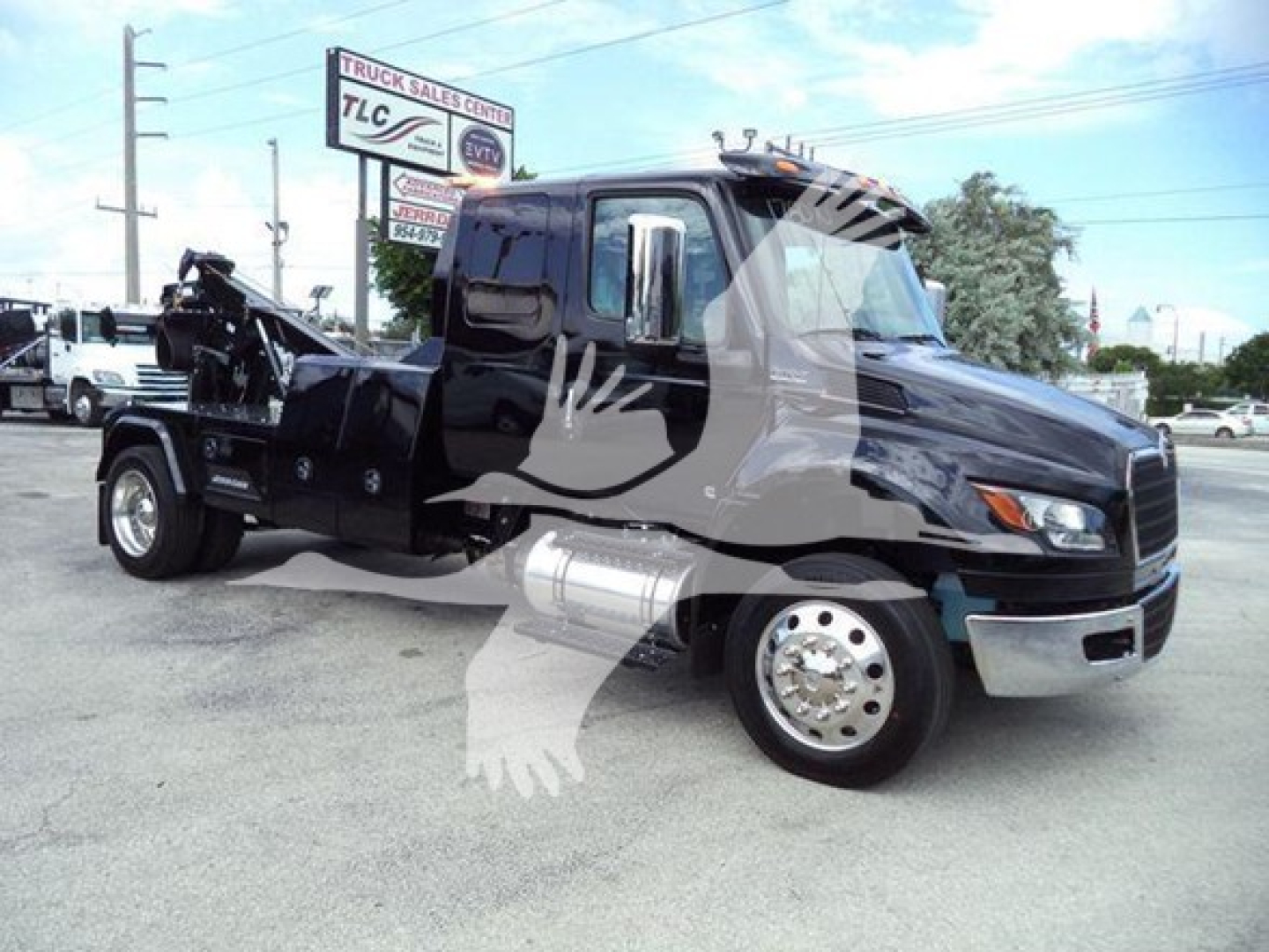 International MV truck with lifting equipment on flatbed, black cab, chrome bumper, visible side mirrors and wheel hub; dealership lot in background.