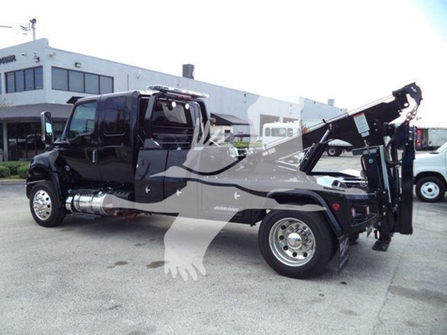 Truck in service bay with crane/winch attachment at rear, black paint, chrome fuel tanks, dual rear wheels, International MV model likely with winch system visible.