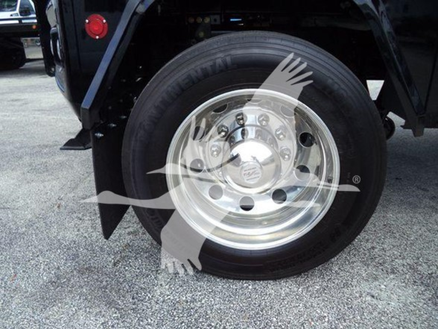 Wheel and tire close-up on a truck, chrome hub with lug nuts visible, part of the fender and chassis in the background.