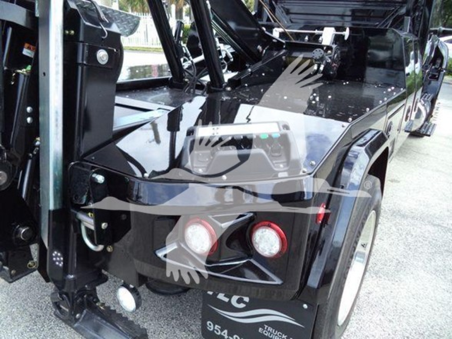 Front-left view of a 2025 International MV truck showing winch setup. Visible: dual round headlights, black glossy hood, metal brackets, winch fairlead, and hydraulic arms.