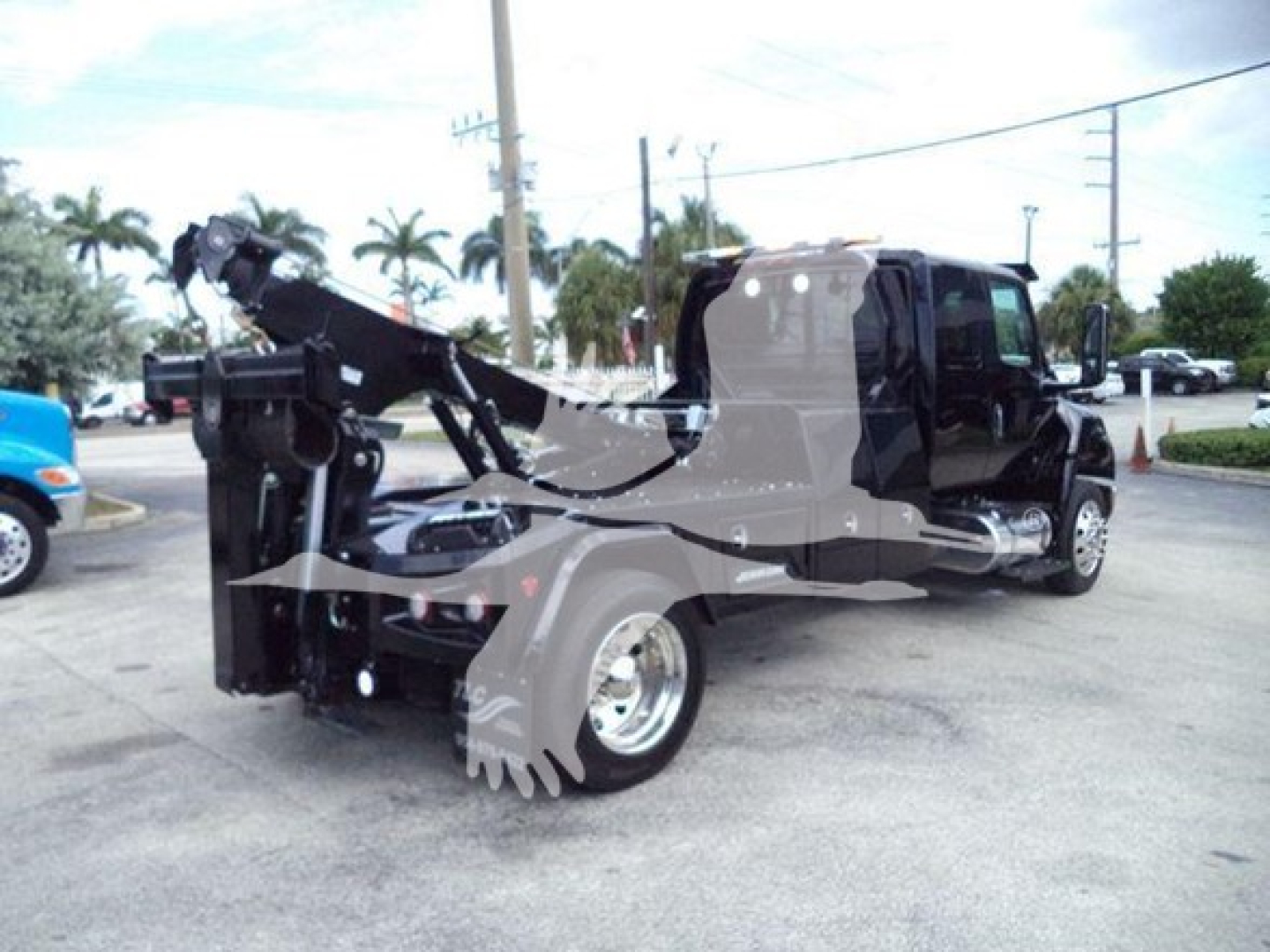 Tow truck with a winch setup on a 2025 International MV, black cab, chrome wheel, winch mechanism at rear, hydraulic lines and control levers visible.