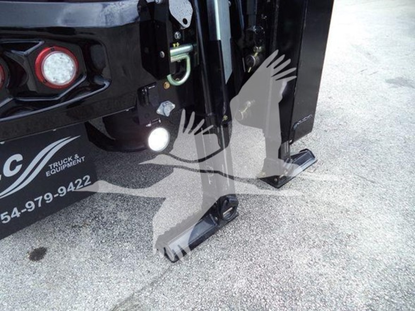 International MV winch truck front hitch and hydraulic components visible on black chassis, close-up of footpad and lifting mechanism.