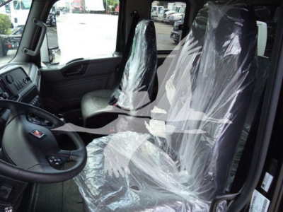 Interior of a new International MV truck cabin with plastic seat coverings, steering wheel visible, dashboard and driver seat in clear view.