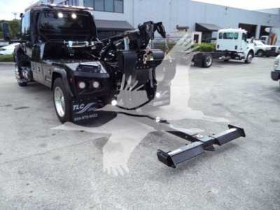Truck with winch in back showing International MV, front view, winch equipment extended on hitch, salvage yard background.