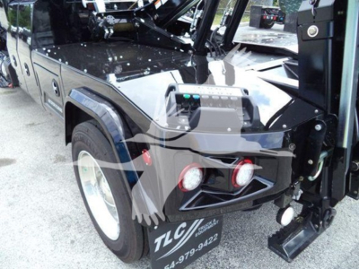 Truck front quarter showing winch mount and control box on International MV, black paint, TLC branding on bumper, large off-road tires.