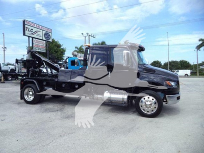 Mercedes-style cab-over International MV tow truck with a winch bed and chrome fuel tanks visible in the chassis area.