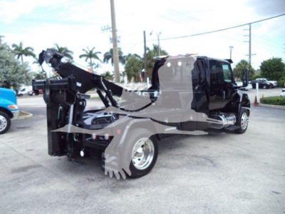 Tow truck with a winch setup on a 2025 International MV, black cab, chrome wheel, winch mechanism at rear, hydraulic lines and control levers visible.